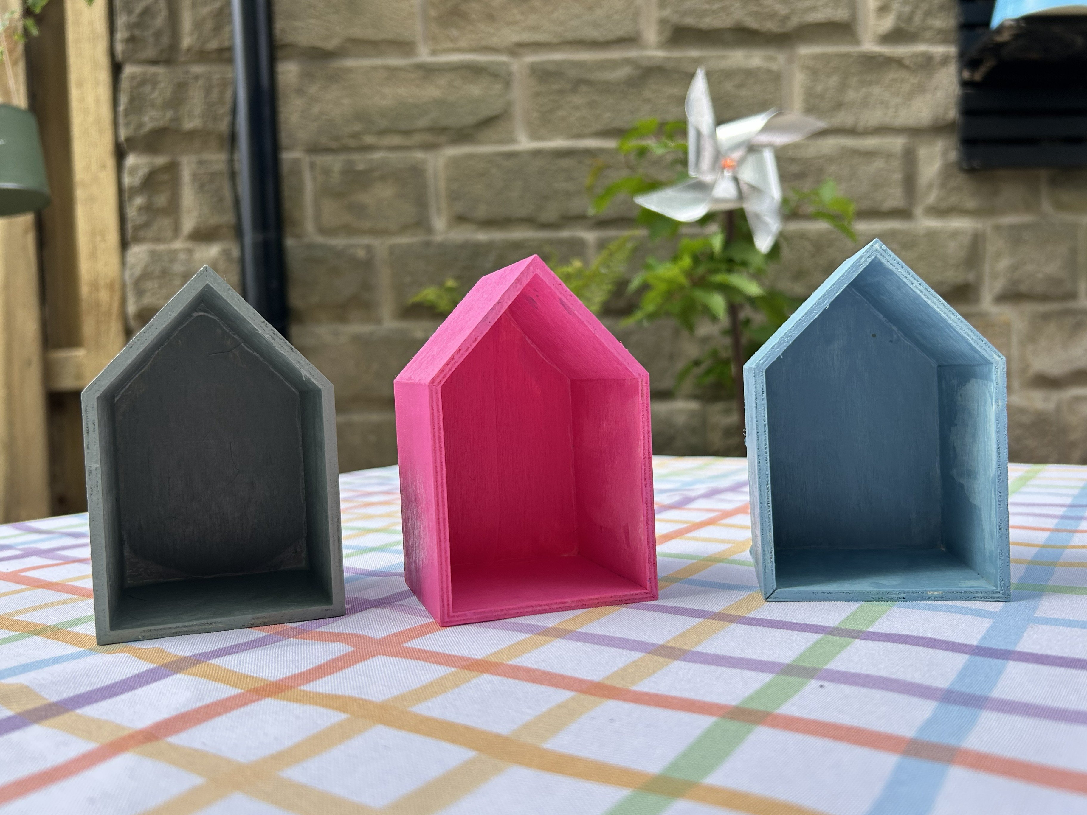 DIY Bug Hotel Outside of the three wooden houses painted in pink, green, and blue.