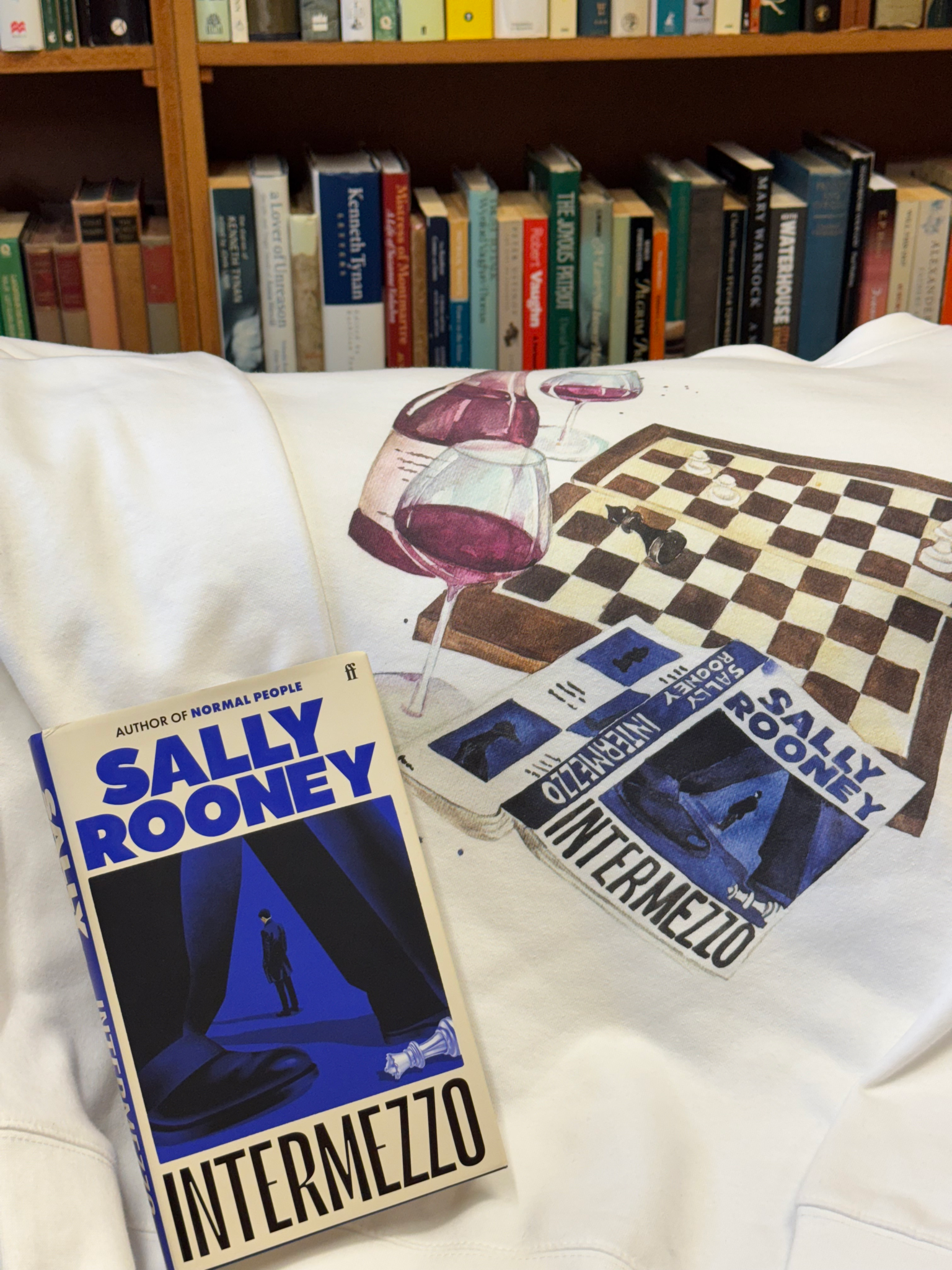 The blue and white book sits on a white hoodie with a print of a chessboard, wine glass, and the book Intermezzo.