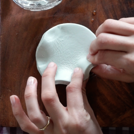 Hands are shaping the outer edge of the clay into a ruffle.