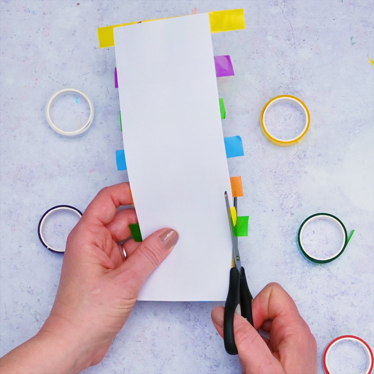 Washi Tape Bookmark White card with excess strips of washi tape being cut with scissors.