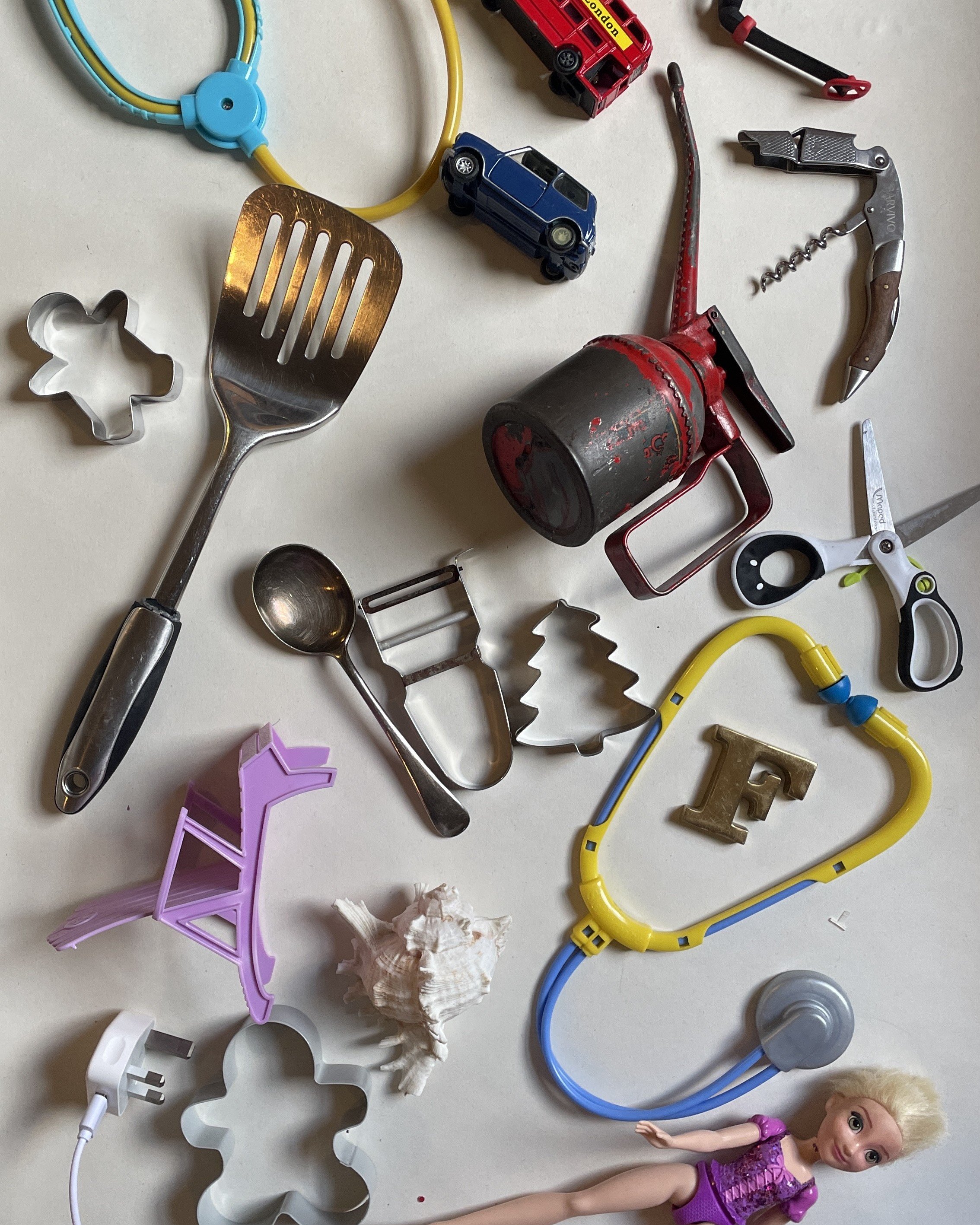 Household items, including toys, oil can, plug, spatula etc., are laid on a large piece of paper.