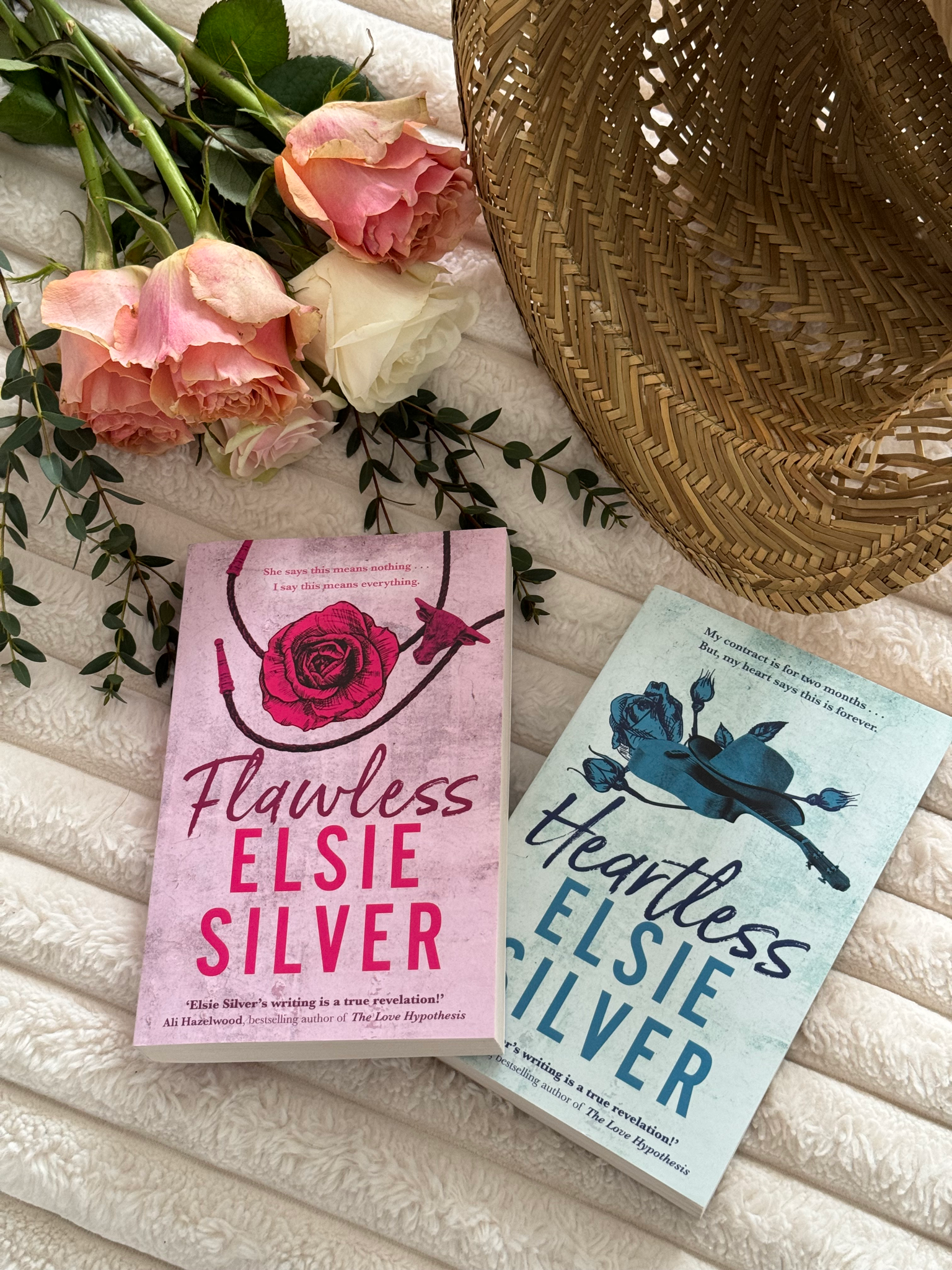 Flawless and Heartless by Elsie Silver sit next to a bunch of pink and white roses and a straw hat.