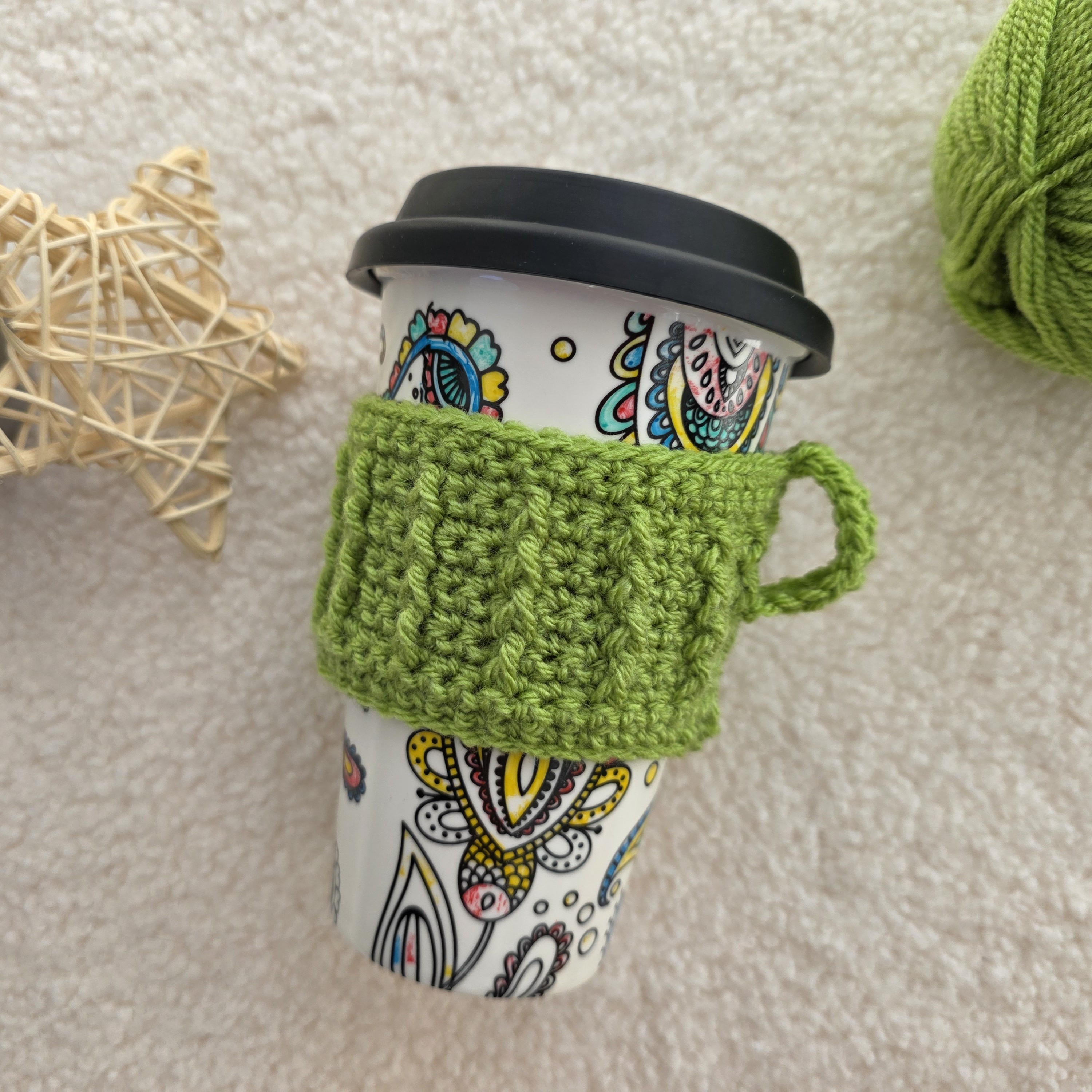 A crocheted green mug cosy around a portable mug.
