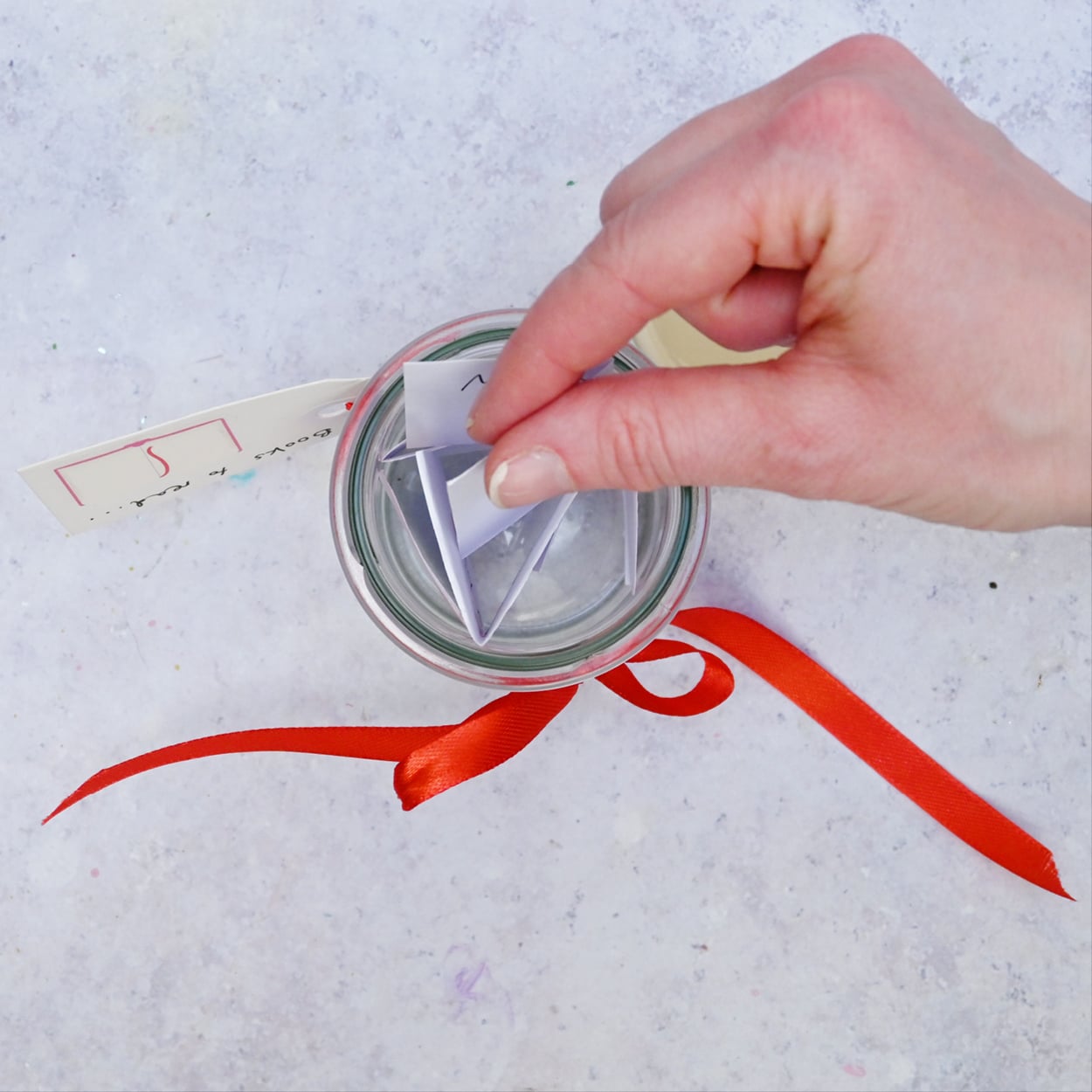 DIY TBR Book Jar A hand places paper into the clear jar.