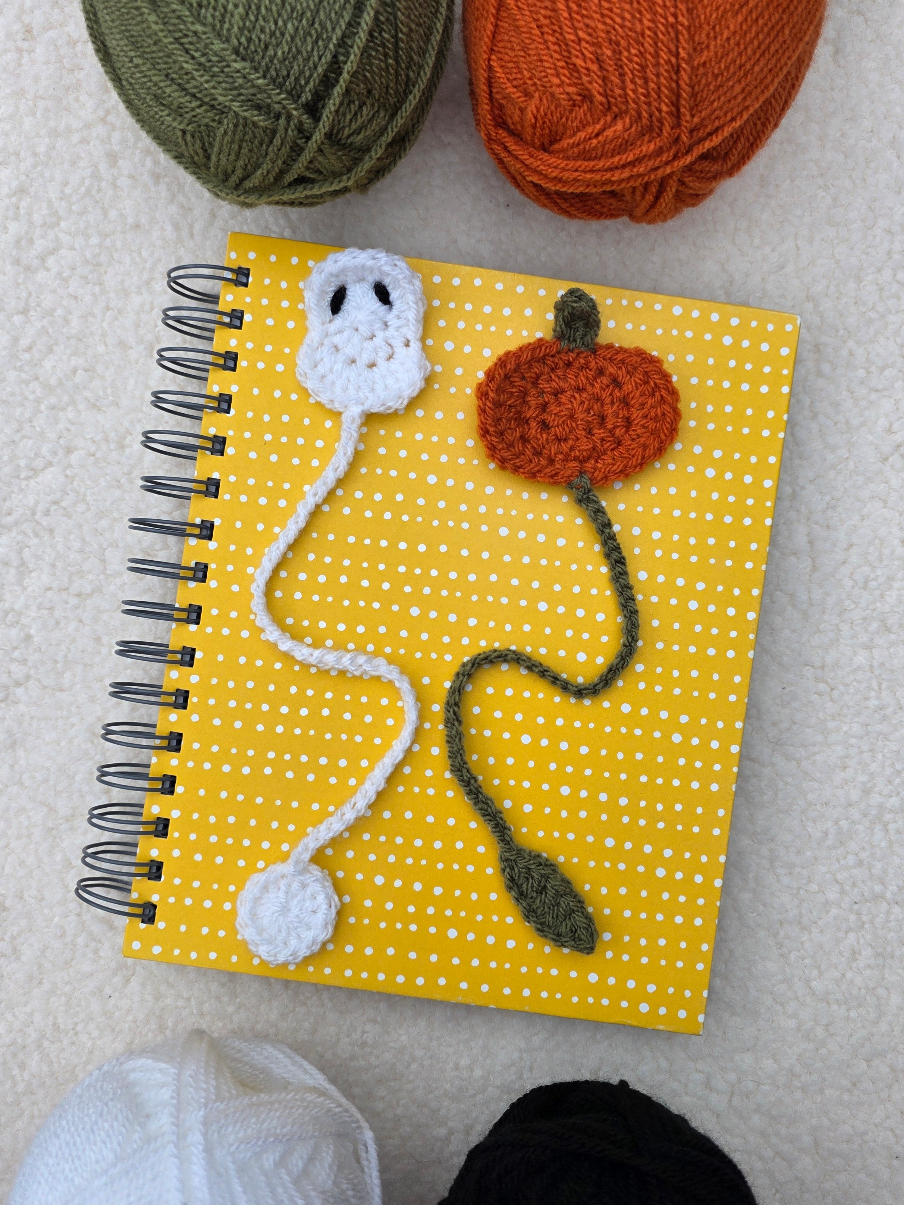 Overhead shot of crochet ghost and crochet pumpkin bookmarks on a yellow notebook.