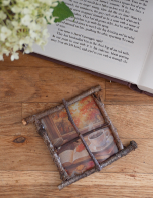 How to Make Your Autumn Window Light Catcher Autumn sticker with twig frame lying on a table next to an open book.