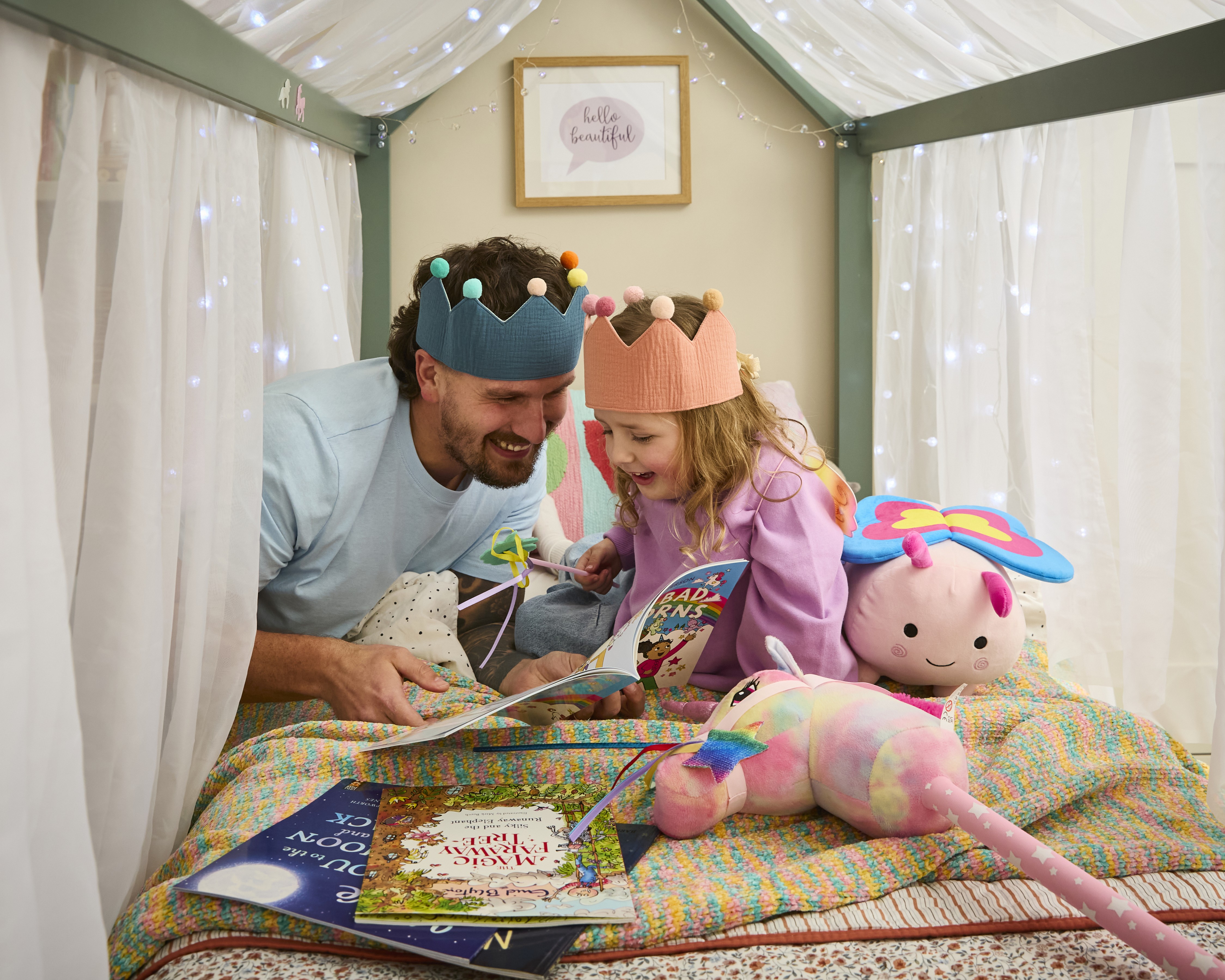 Dad and daughter wearing crowns in bed reading a bedtime story together.