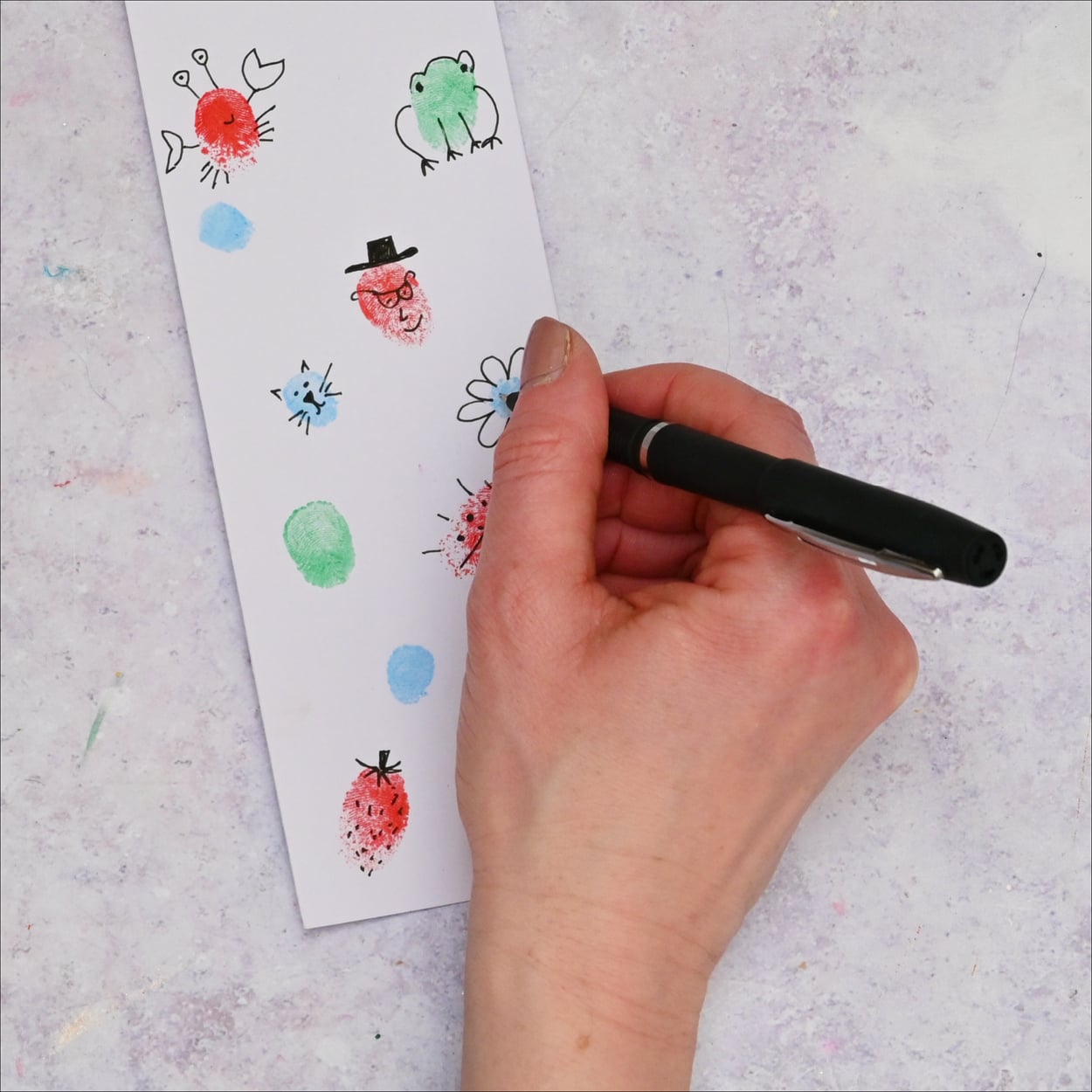 Black fine liner is drawing faces onto the colourful fingerprints.
