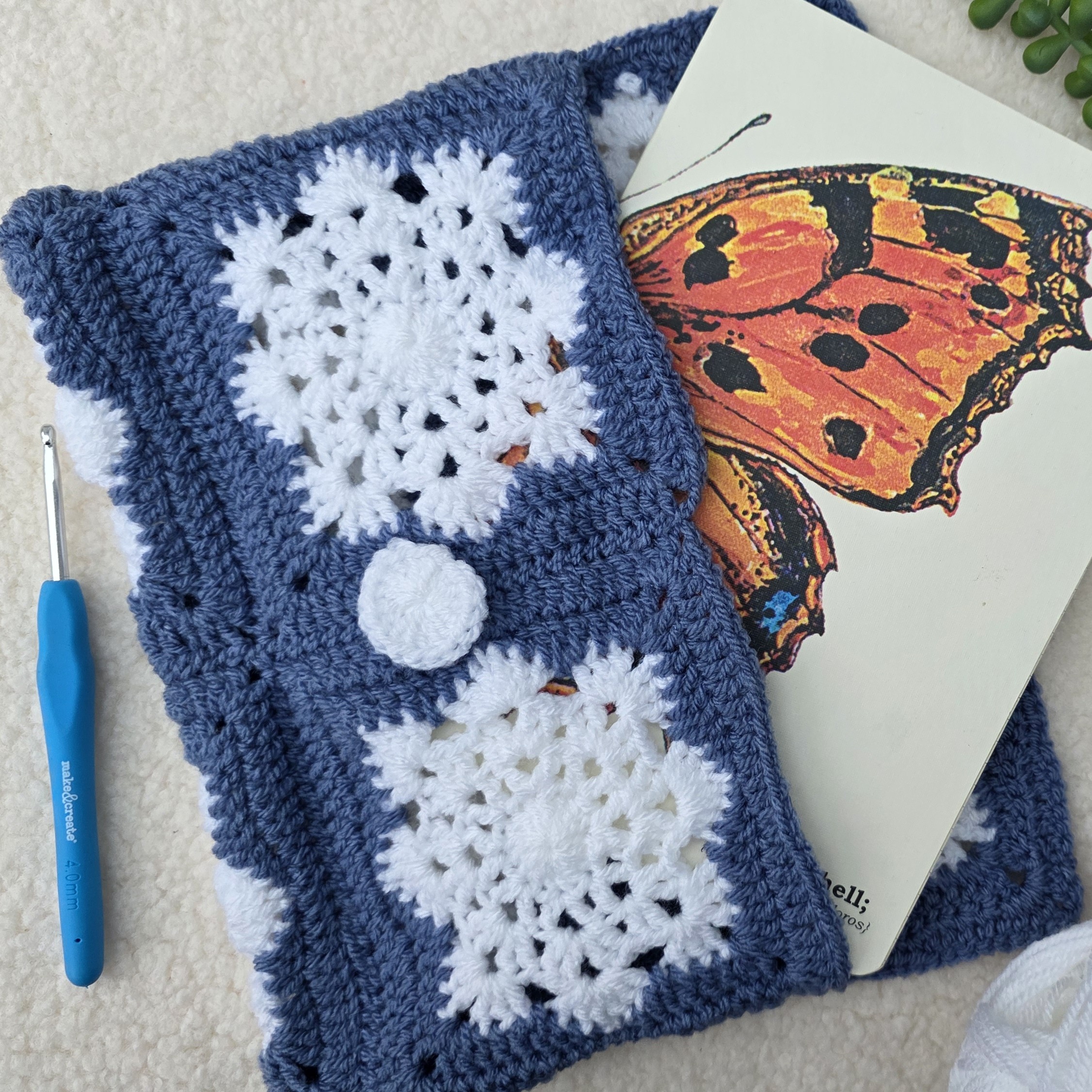 A blue and white crocheted book sleeve made with snowflake granny squares.