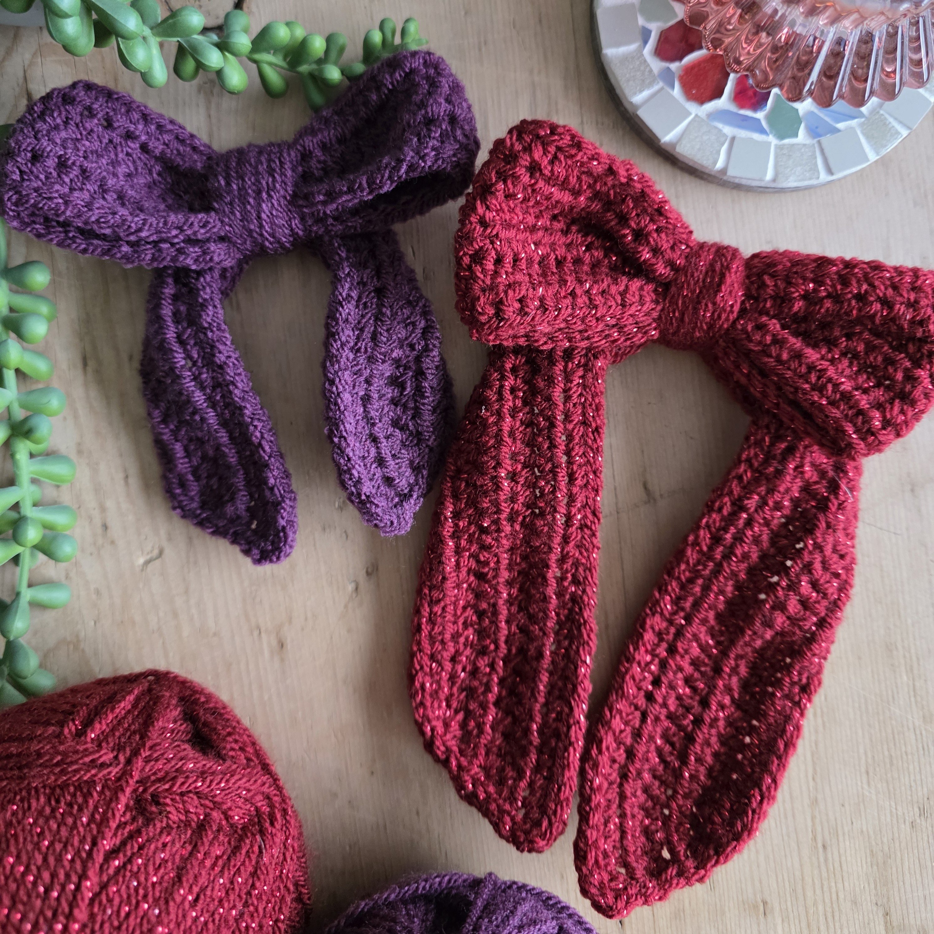 A large burgundy crochet bow sits next to a smaller plum-coloured crochet bow on a table.