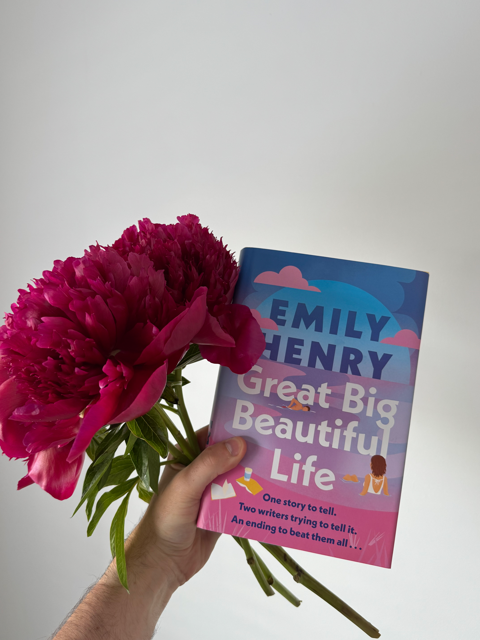 The colourful book is held up next to a bunch of pink flowers.