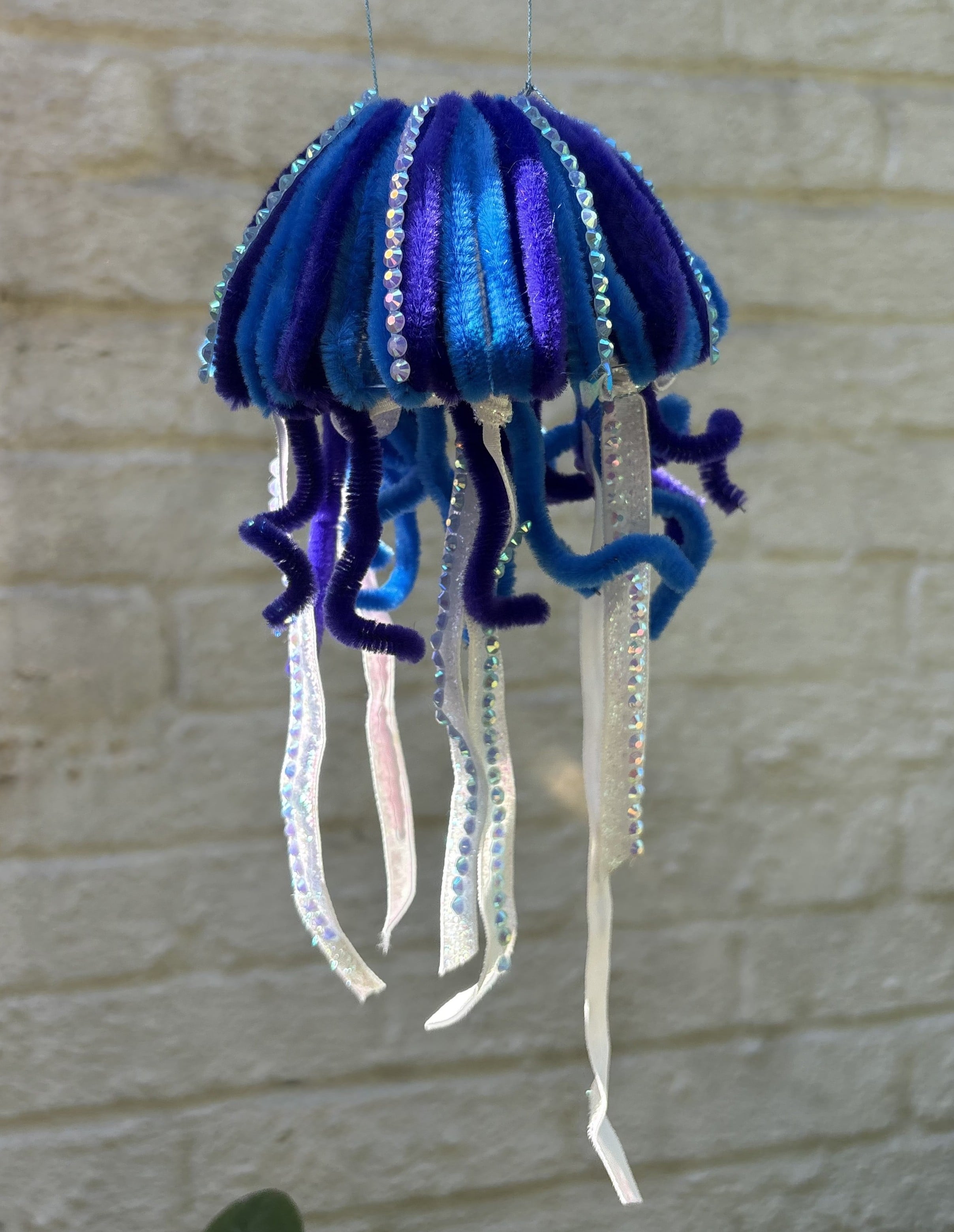 Blue and purple pipe cleaner jellyfish with white ribbon tentacles and sparkles. 
