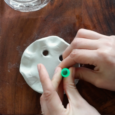 Hands holding straw to create holes in the clay.