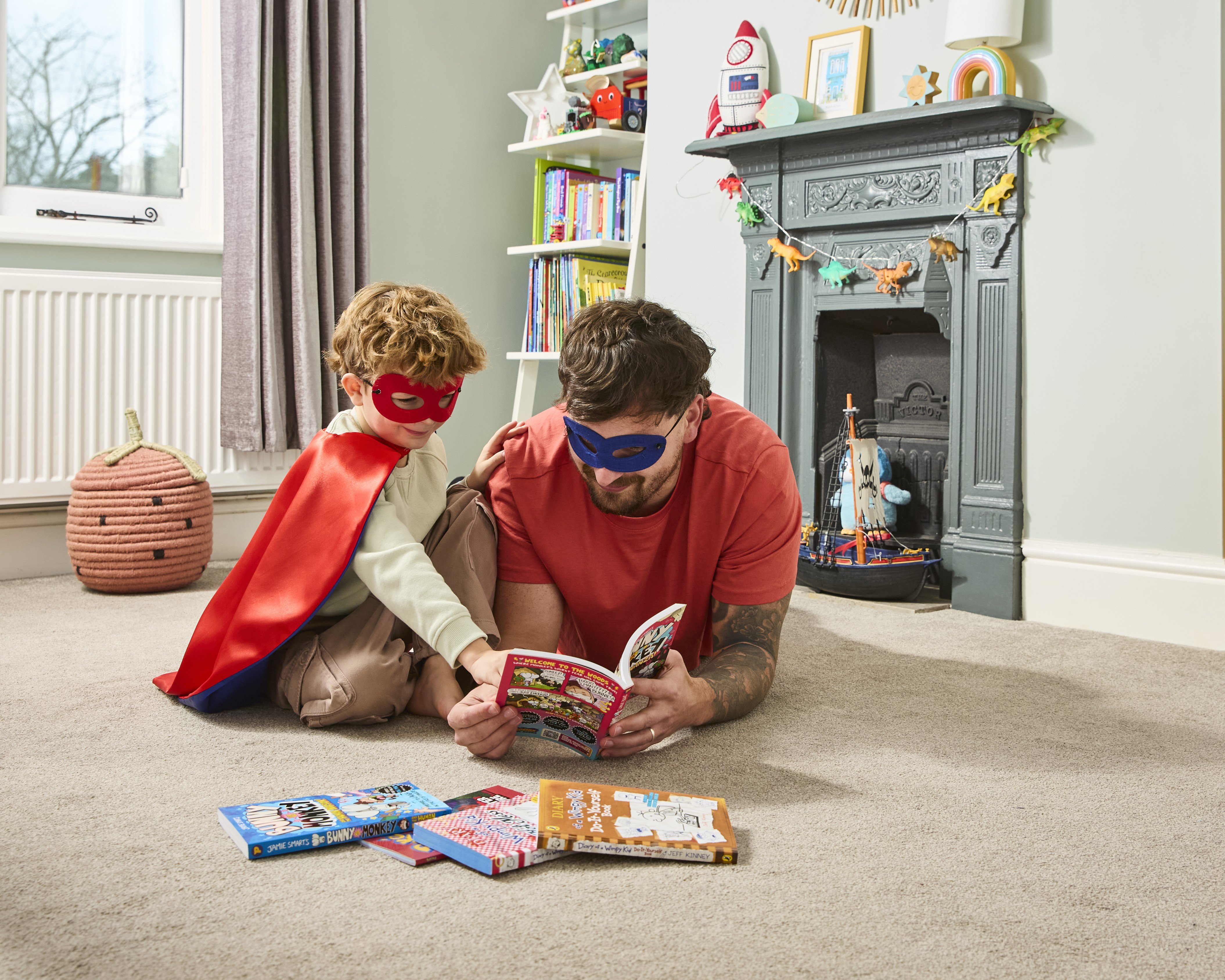 Dad and son dresses as superheroes reading a graphic novel together.